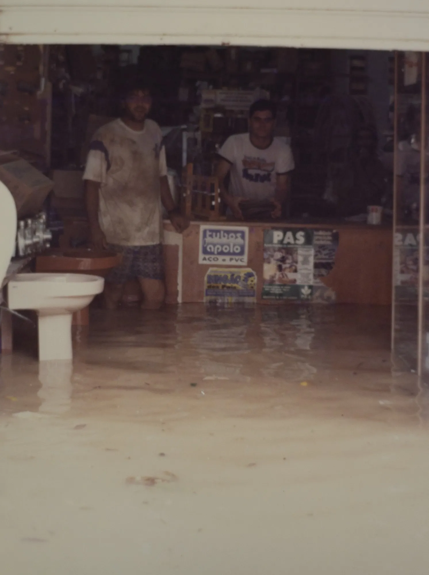 Uma das enchentes do Rio Doce: a loja com água pelos joelhos e a equipe no balcão.